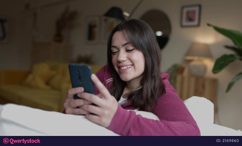 Pretty young adult woman using mobile phone while relaxing on sofa at home video 2169860
